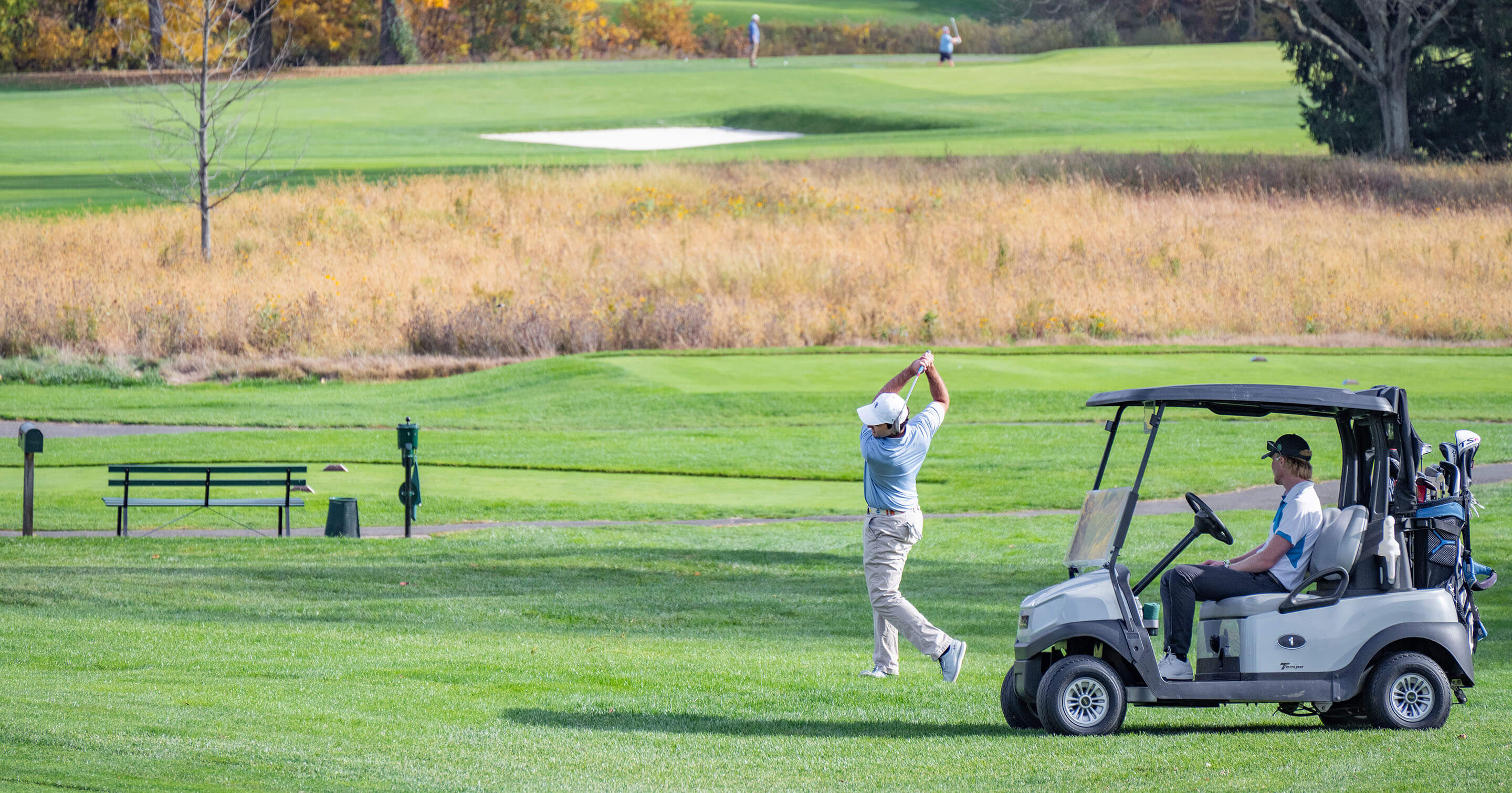 golfer swinging club in front of golf cart